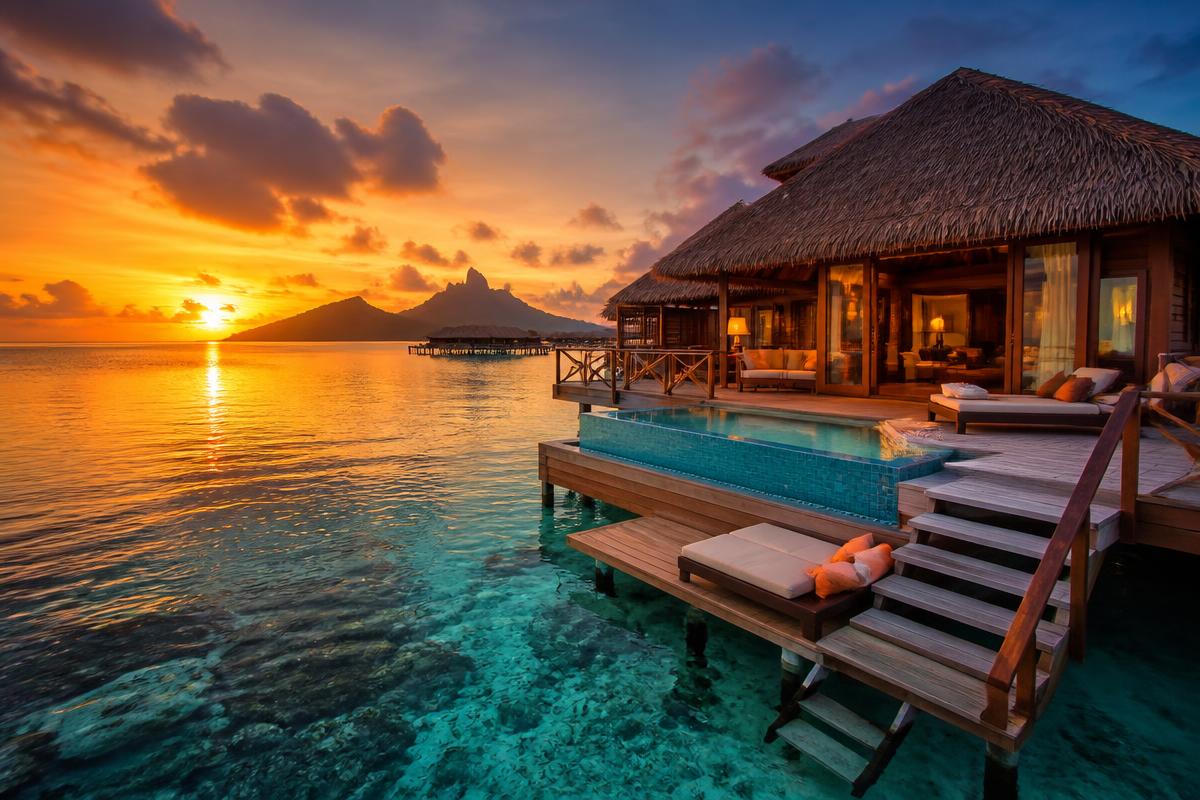 Luxury tropical overwater bungalow at sunset with crystal clear water